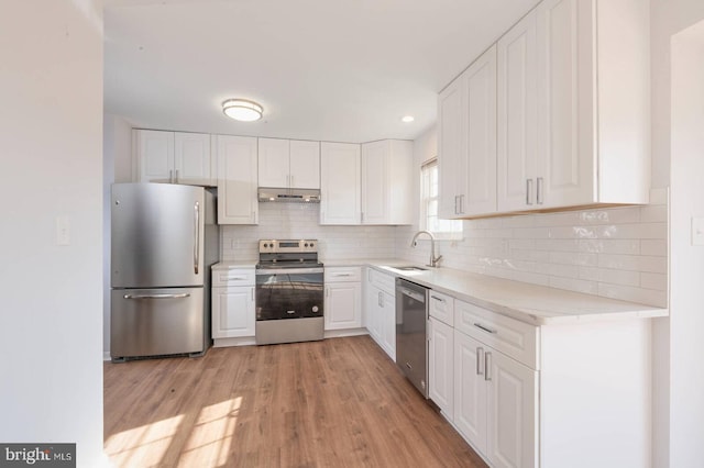 kitchen featuring under cabinet range hood, light wood-style flooring, appliances with stainless steel finishes, white cabinets, and a sink