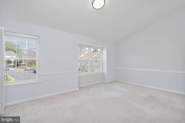 carpeted spare room featuring lofted ceiling and baseboards