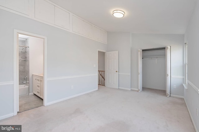 unfurnished bedroom featuring baseboards, vaulted ceiling, a closet, ensuite bathroom, and light colored carpet