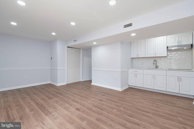 interior space with visible vents, white cabinets, light wood-style floors, under cabinet range hood, and backsplash