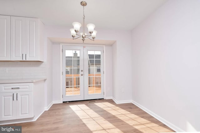 unfurnished dining area with light wood-type flooring, french doors, baseboards, and a chandelier