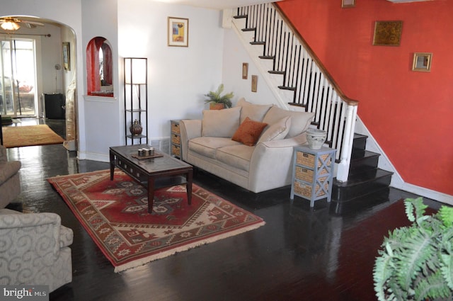 living room with arched walkways, a ceiling fan, wood finished floors, baseboards, and stairs