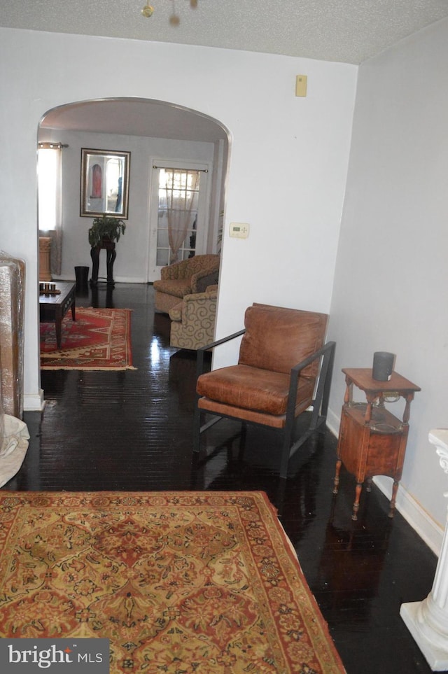 interior space featuring arched walkways, a textured ceiling, wood finished floors, and baseboards