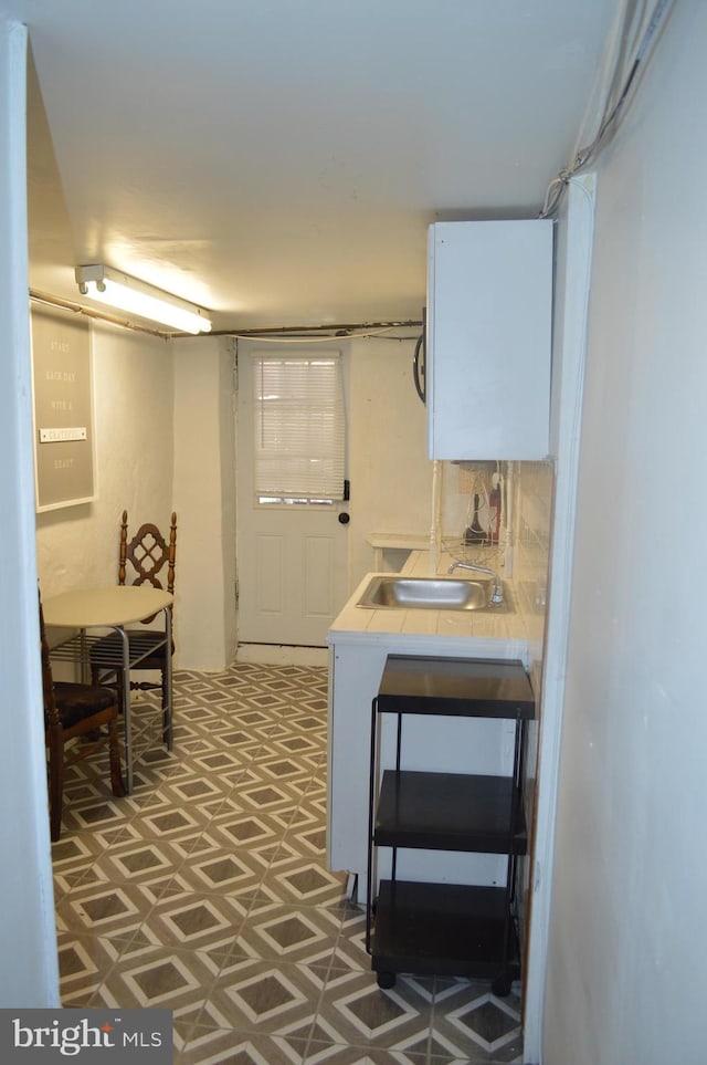 kitchen featuring white cabinetry, tile counters, and a sink