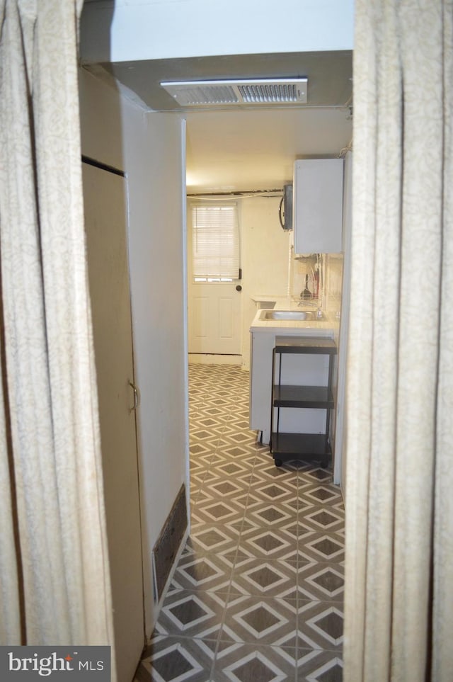 corridor featuring light floors, visible vents, and a sink