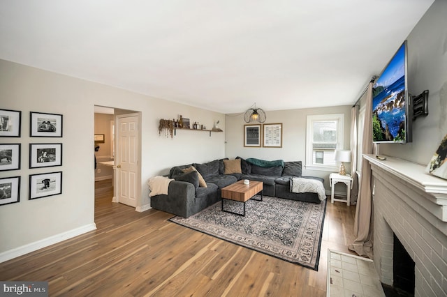 living area featuring a brick fireplace, wood finished floors, and baseboards