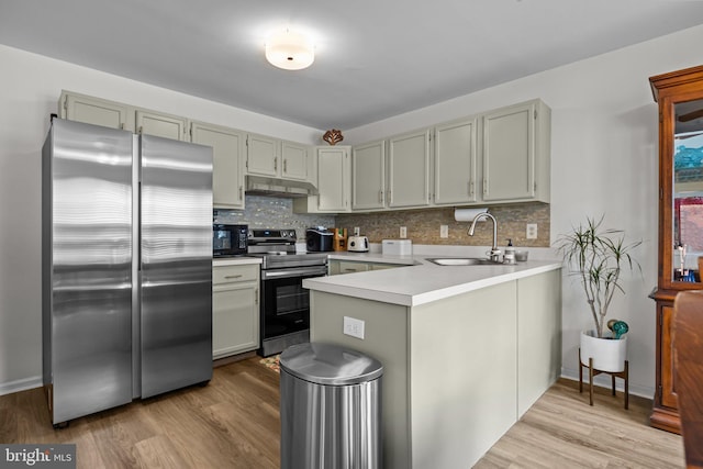 kitchen with under cabinet range hood, stainless steel appliances, a peninsula, a sink, and tasteful backsplash