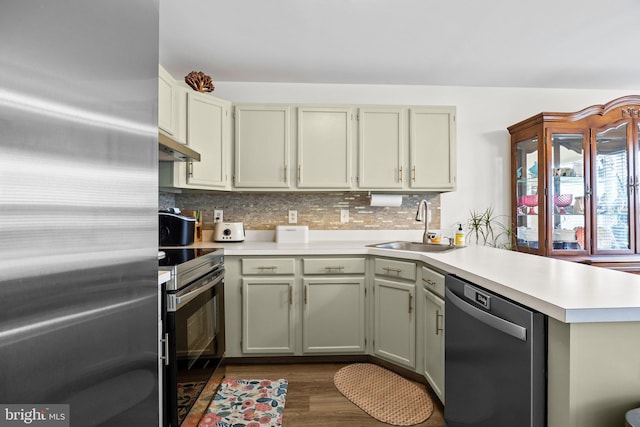 kitchen with stainless steel appliances, a peninsula, a sink, light countertops, and decorative backsplash