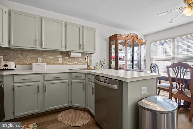 kitchen featuring a peninsula, a sink, light countertops, stainless steel dishwasher, and backsplash