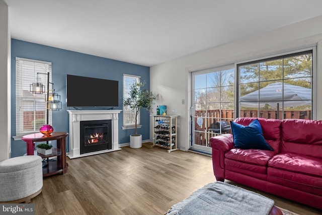 living room featuring a glass covered fireplace, wood finished floors, and baseboards