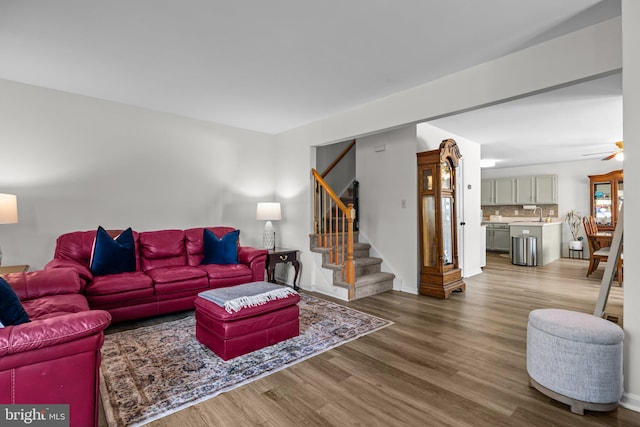 living room with baseboards, ceiling fan, stairway, and wood finished floors