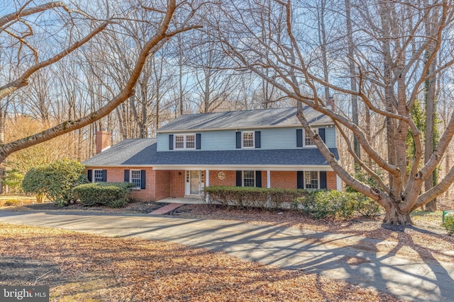 view of front facade featuring covered porch, a shingled roof, concrete driveway, and brick siding