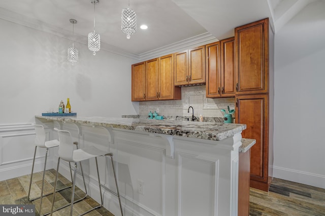 856 N Harrison St, Arlington, VA 22205 - kitchen featuring decorative backsplash, brown cabinetry, a kitchen bar, pendant lighting, and ornamental molding