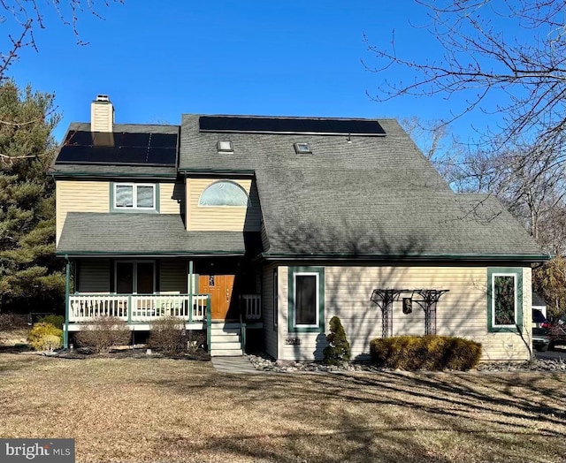 view of front facade with a porch, a chimney, and roof mounted solar panels