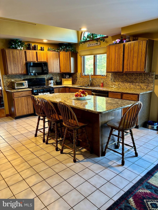 kitchen featuring black appliances, a kitchen bar, brown cabinets, and a sink