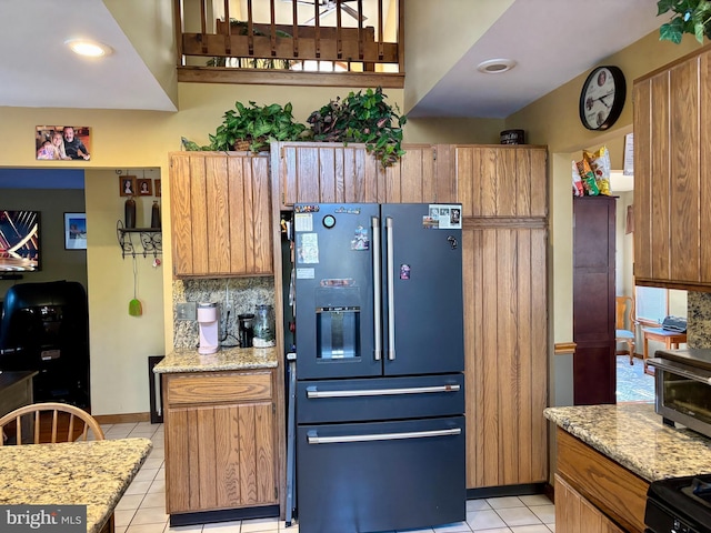 kitchen featuring decorative backsplash, light stone counters, brown cabinets, fridge with ice dispenser, and light tile patterned flooring