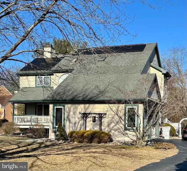 view of front of property with covered porch, roof with shingles, and a chimney