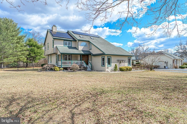 view of front of house featuring roof with shingles, a chimney, solar panels, a porch, and a front yard