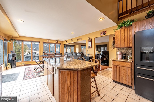 kitchen with light tile patterned floors, brown cabinetry, a kitchen bar, and black fridge with ice dispenser