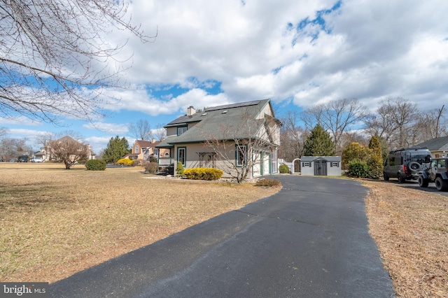 view of side of property featuring an outbuilding, a chimney, a lawn, a garage, and driveway