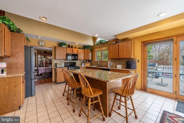 kitchen with brown cabinetry, a breakfast bar, a sink, and black appliances