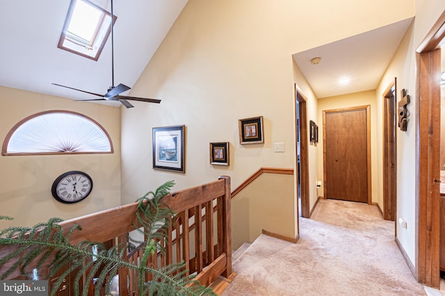 hallway featuring a skylight, light colored carpet, an upstairs landing, high vaulted ceiling, and baseboards