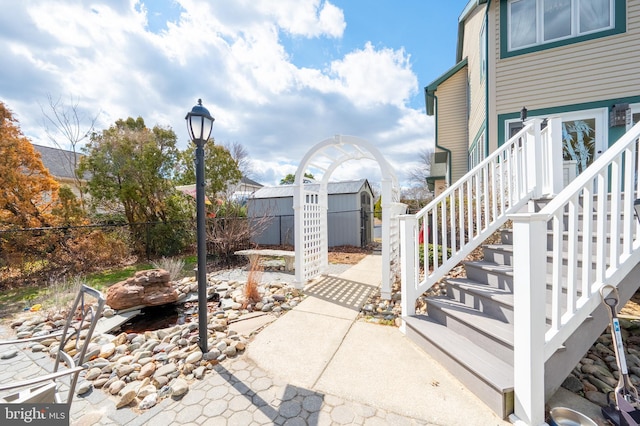 view of patio featuring stairs, an outbuilding, fence, and a storage unit