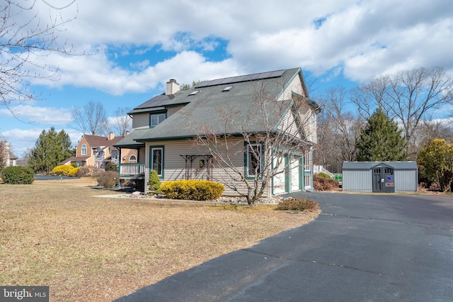 view of side of property featuring a yard, a chimney, roof mounted solar panels, a garage, and driveway