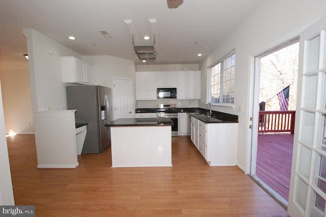 kitchen featuring stainless steel appliances, a sink, white cabinetry, light wood-type flooring, and dark countertops