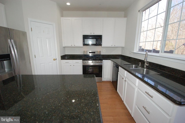 kitchen with light wood-style flooring, white cabinets, a sink, dark stone countertops, and black appliances