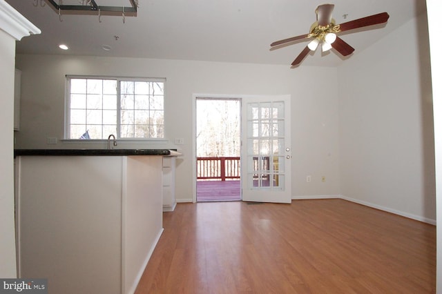 interior space with ceiling fan, a sink, baseboards, light wood-type flooring, and dark countertops