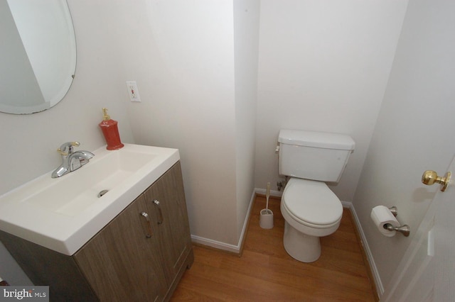 half bathroom featuring baseboards, vanity, toilet, and wood finished floors