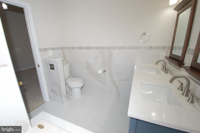 bathroom with a sink, tile walls, toilet, and double vanity