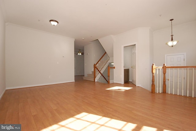 empty room featuring baseboards, a ceiling fan, light wood-style flooring, stairway, and crown molding