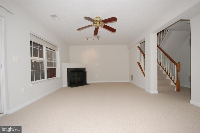 unfurnished living room featuring ceiling fan, carpet floors, a fireplace with flush hearth, baseboards, and stairway