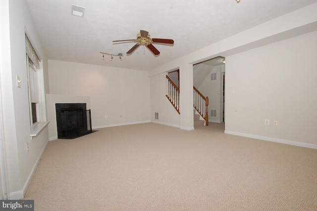 unfurnished living room featuring visible vents, a fireplace with flush hearth, ceiling fan, baseboards, and stairs