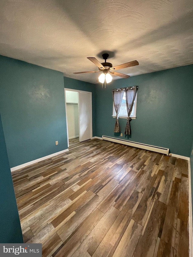 spare room with baseboards, a baseboard heating unit, ceiling fan, and wood finished floors