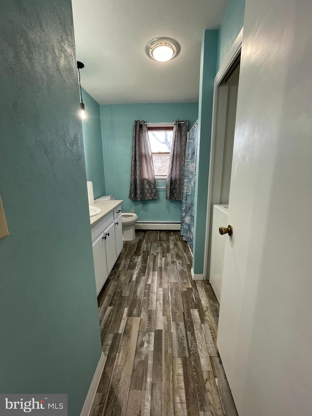 bathroom featuring toilet, a shower with curtain, wood finished floors, vanity, and a baseboard heating unit