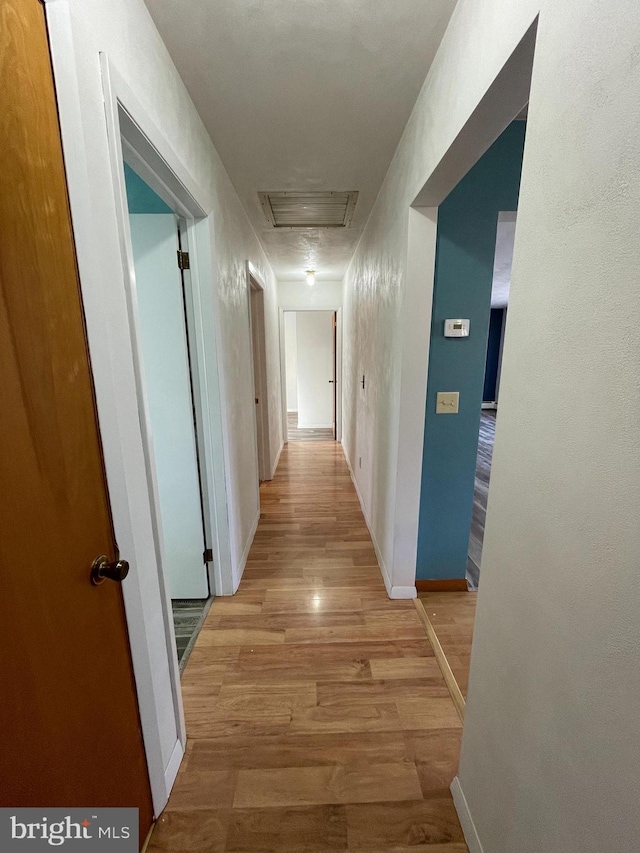 corridor with attic access, baseboards, visible vents, and light wood finished floors