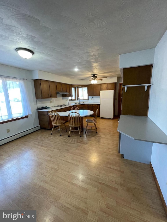 kitchen featuring light countertops, freestanding refrigerator, a sink, under cabinet range hood, and a kitchen bar