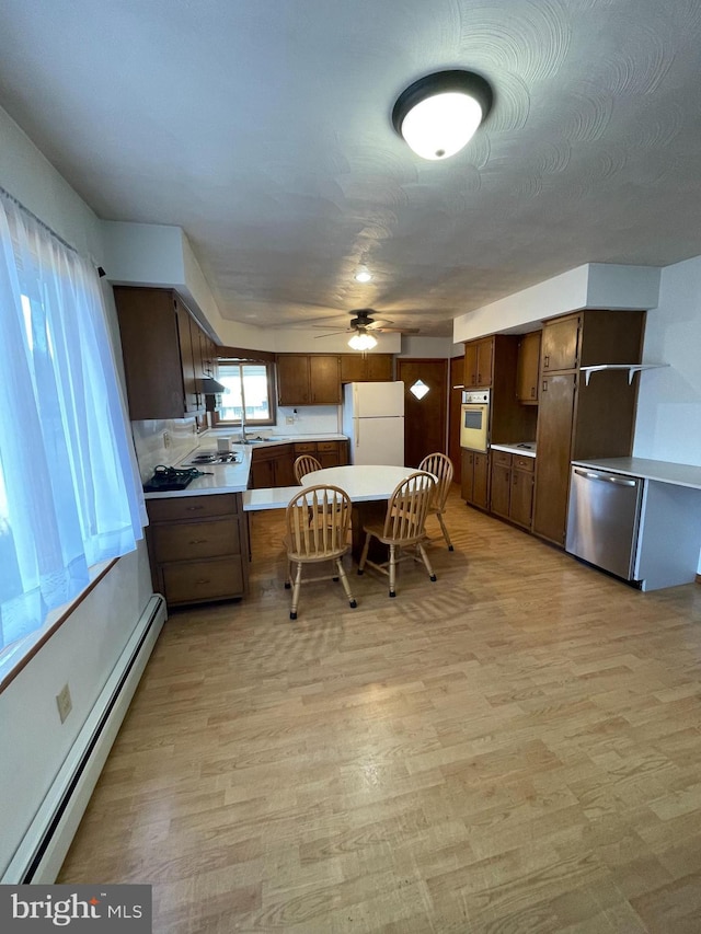 kitchen featuring white appliances, a baseboard radiator, light countertops, light wood-style floors, and a sink