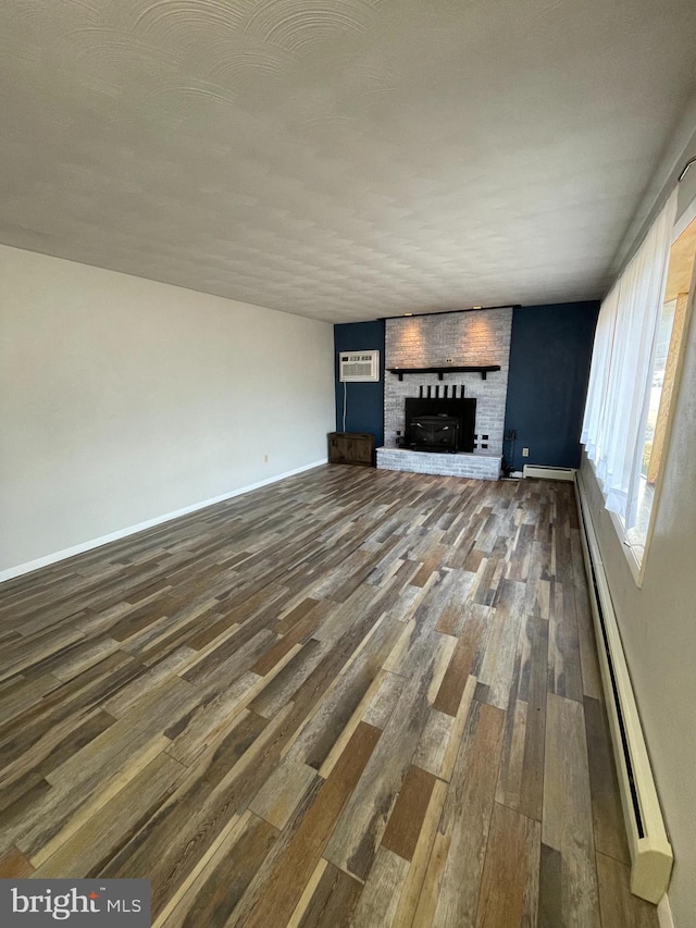 unfurnished living room with a baseboard heating unit, a brick fireplace, wood finished floors, and baseboards