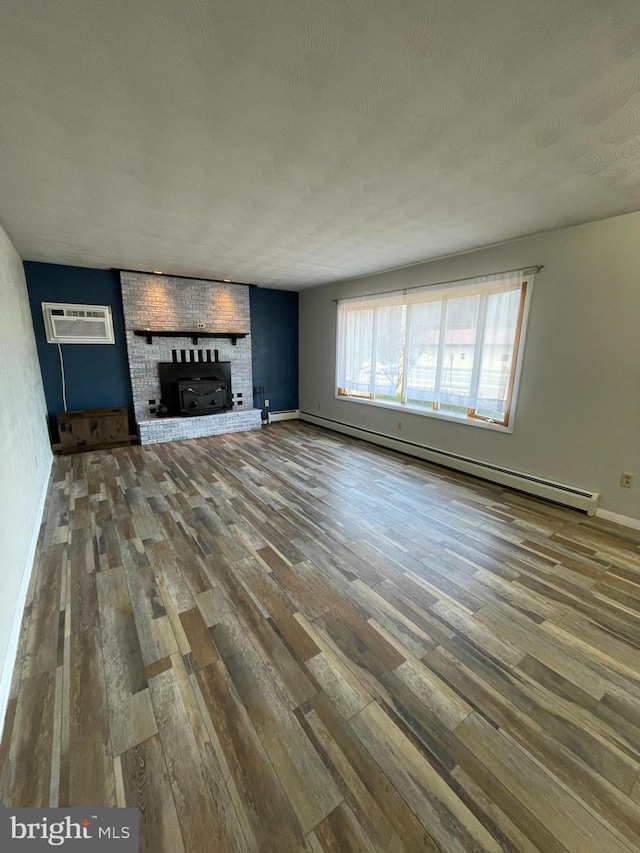 unfurnished living room with a baseboard heating unit, an AC wall unit, a brick fireplace, and wood finished floors