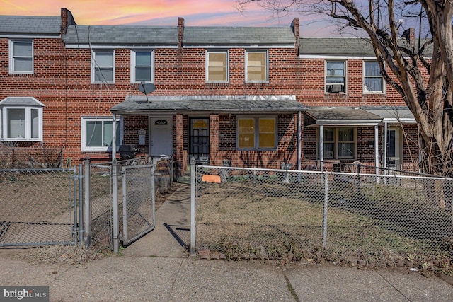 townhome / multi-family property featuring a fenced front yard, covered porch, brick siding, and a gate