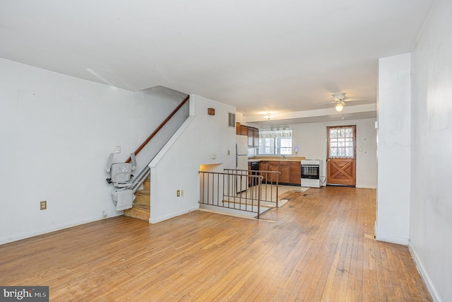 living area featuring ceiling fan, light wood-style flooring, baseboards, and stairs