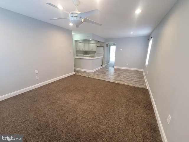 unfurnished living room with ceiling fan, recessed lighting, a sink, baseboards, and dark colored carpet