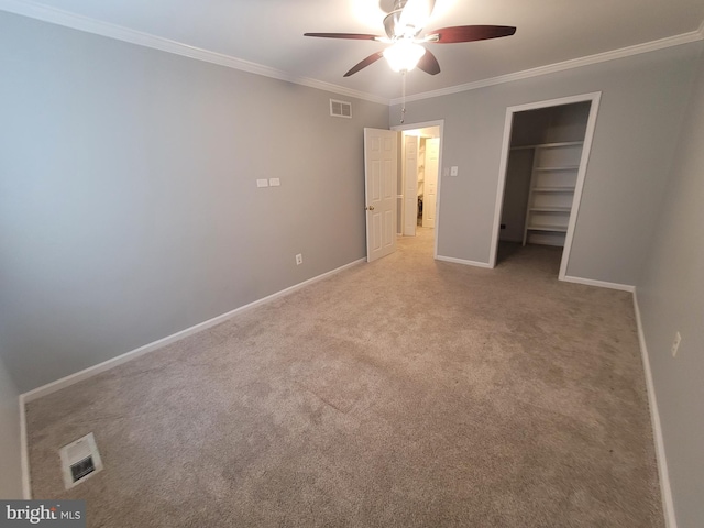 unfurnished bedroom featuring carpet floors, a walk in closet, visible vents, ornamental molding, and baseboards