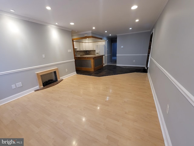 unfurnished living room with ornamental molding, a fireplace with raised hearth, wood finished floors, and recessed lighting