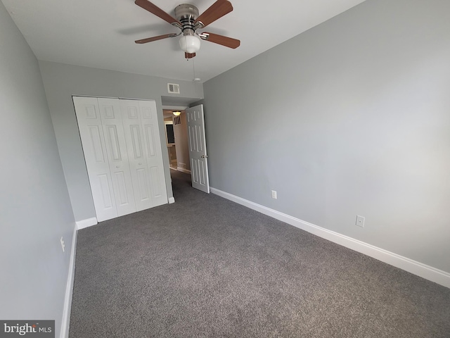 unfurnished bedroom with baseboards, visible vents, dark carpet, and a closet