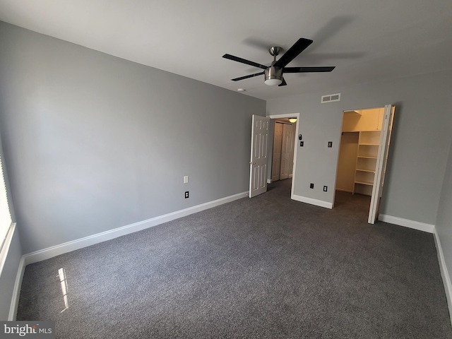 unfurnished bedroom featuring baseboards, visible vents, a ceiling fan, a walk in closet, and dark carpet